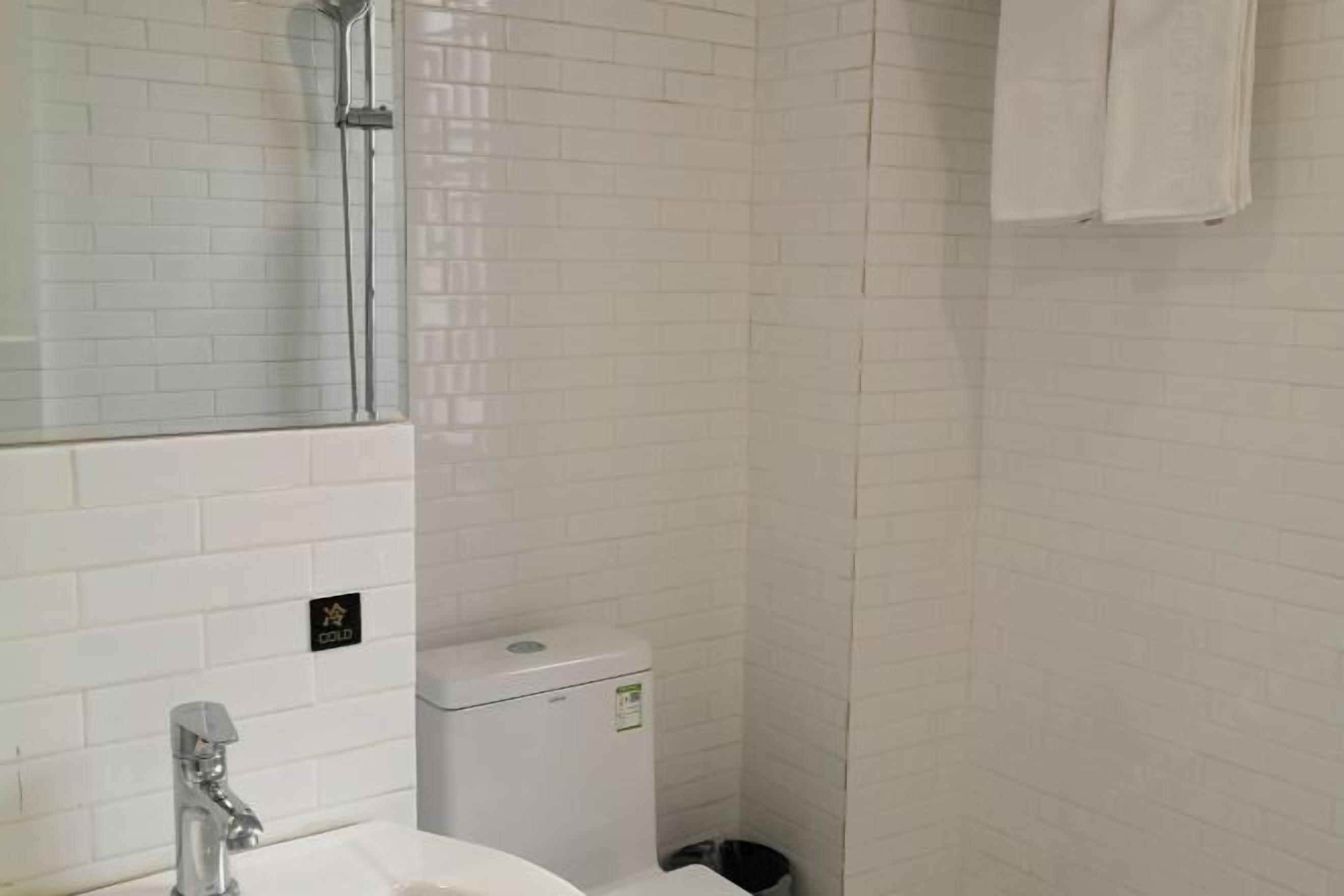 A bathroom with white tiled walls, a white sink, a mirror, and a toilet.