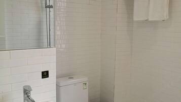 A bathroom with white tiled walls, a white sink, a mirror, and a toilet.