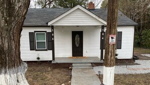 A white single-story house with black shutters, a front door, and a small porch.