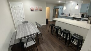 A modern kitchen with a central island, bar stools, and a dining area with a table and chairs.