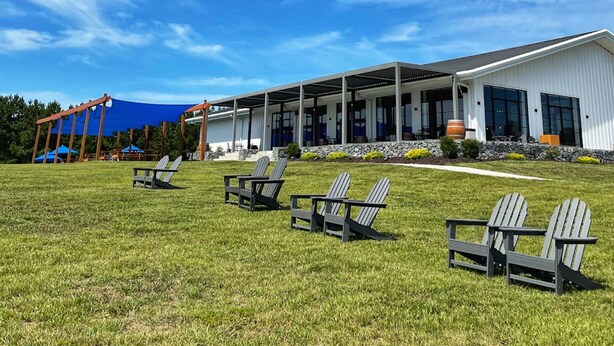 A building with a covered patio area, outdoor seating with Adirondack chairs, and a stone foundation.