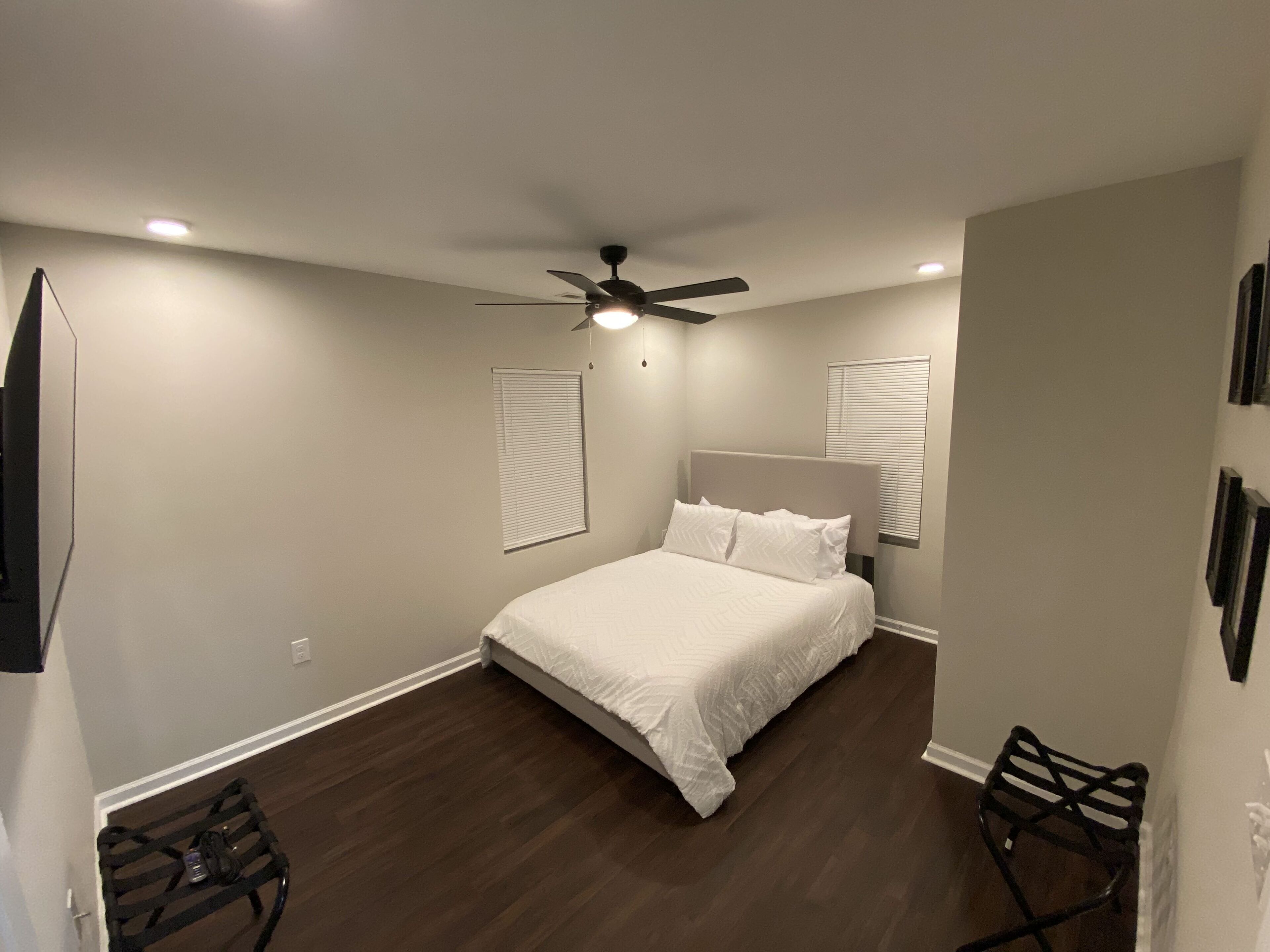 A bedroom with a bed, ceiling fan, and two wall-mounted televisions.