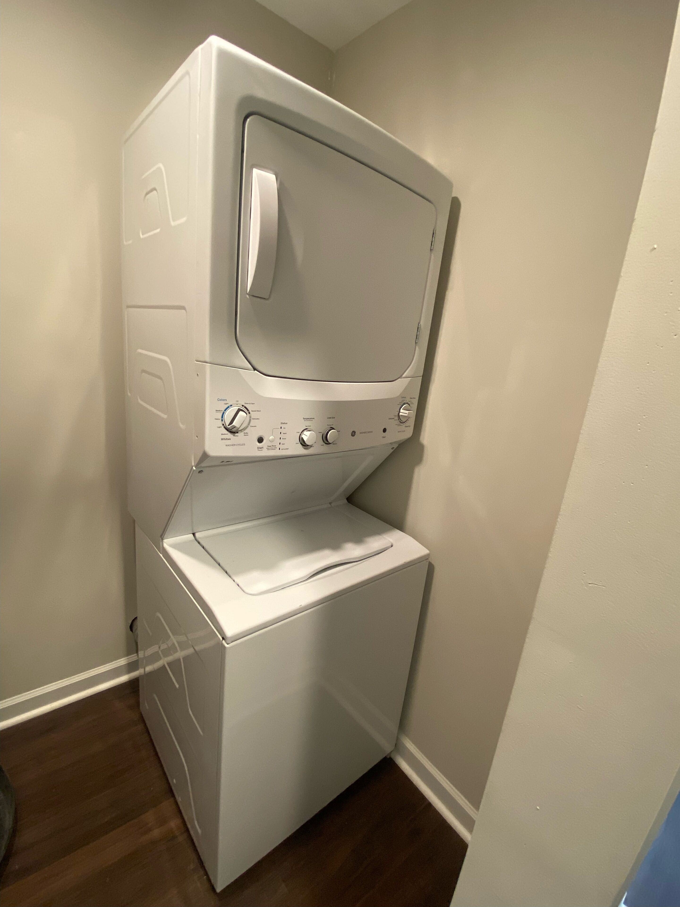 A stacked washer and dryer in a corner with a wooden floor.