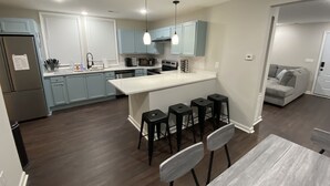 A modern kitchen with light blue cabinets, a central island with bar stools, and a dining area with a table and chairs.