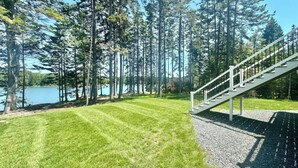 A well-maintained lawn, a staircase leading to a deck, and a lake surrounded by tall trees.