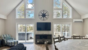 A spacious living area with a large TV, a dining table, and multiple windows.