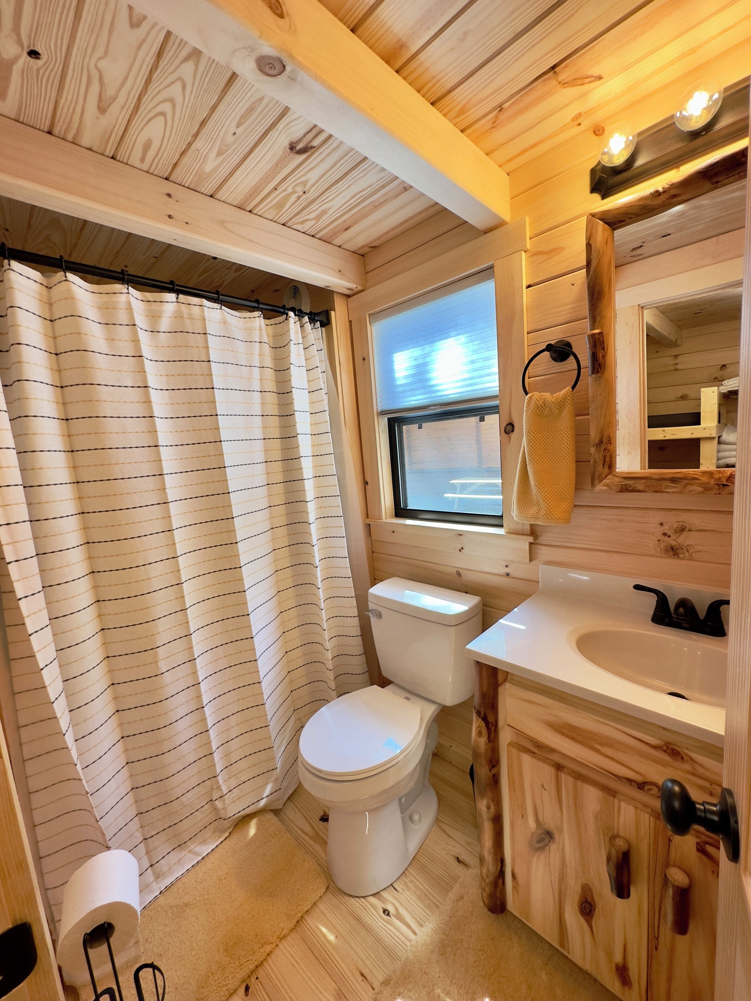 Une petite salle de bain aux finitions en bois, comprenant des toilettes, un lavabo et une fenêtre.