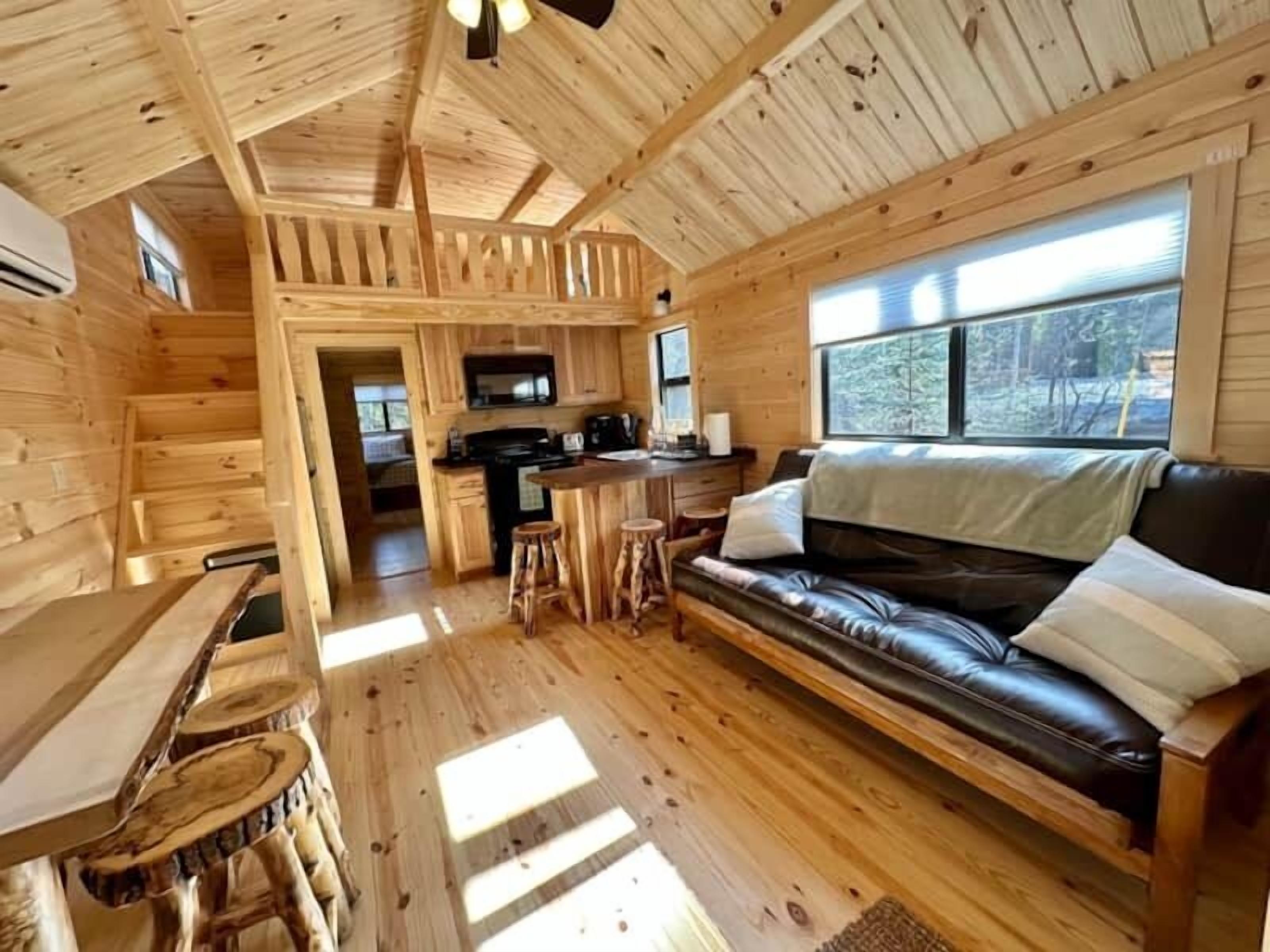 Interior de una cabaña de troncos con cocina, comedor y sala de estar con un sofá de cuero.