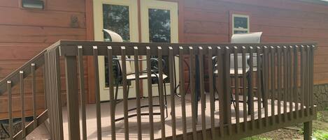 Una terraza de madera con barandilla, un conjunto de sillas de exterior y una mesa.
