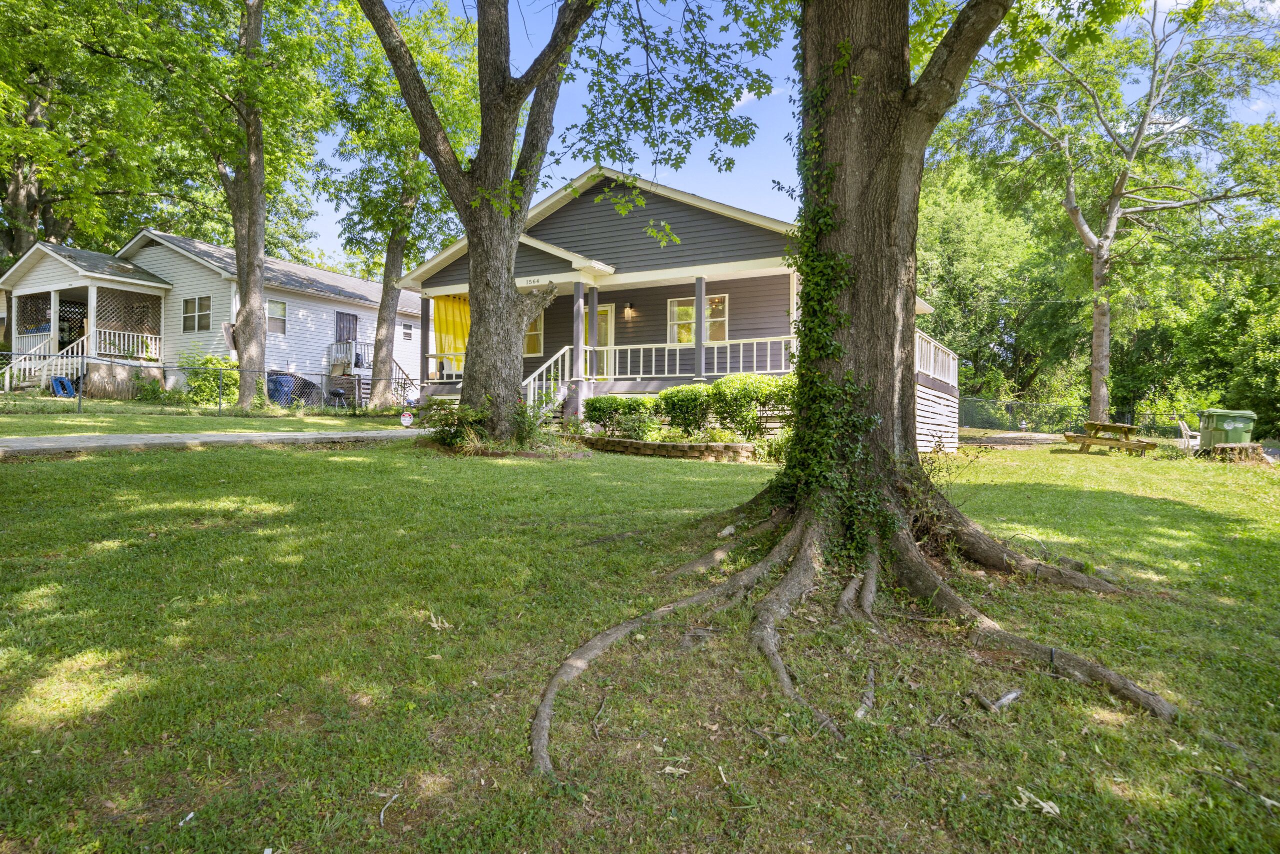 Une maison à deux étages avec un porche, entourée d’arbres et d’une pelouse bien entretenue.