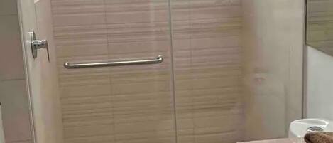 A modern bathroom with a glass shower enclosure, a toilet, and a sink with a countertop.