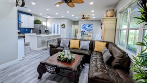 A spacious living room with a brown leather sofa, a wooden coffee table, and a ceiling fan.