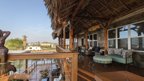 A covered outdoor seating area with wooden furniture and a thatched roof.