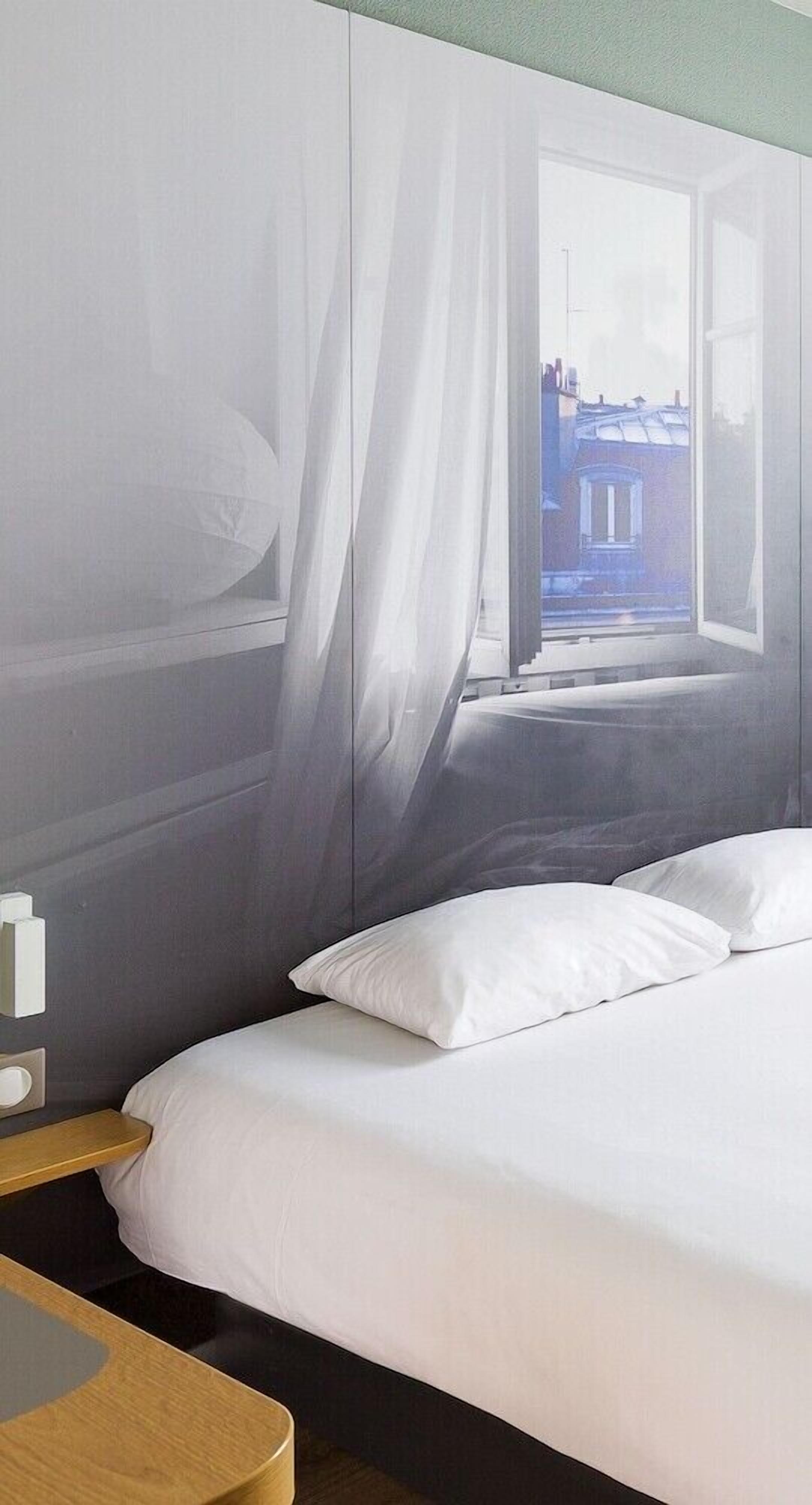 Un dormitorio con cama, mesita de noche y ventana con cortinas.