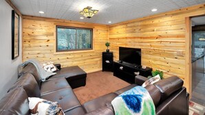 A cozy living room with a large window, a flat-screen TV, and a leather sofa.