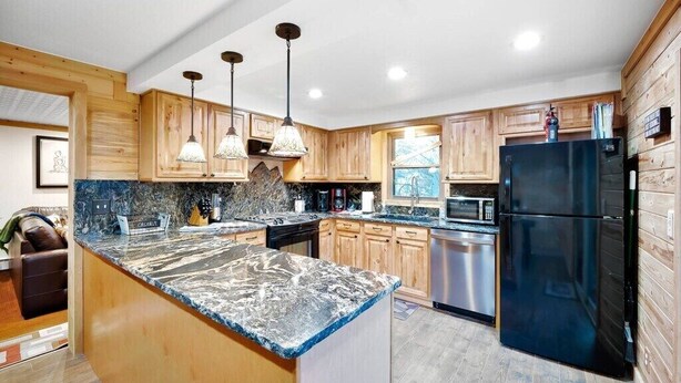 A modern kitchen with wooden cabinets, a granite countertop, stainless steel appliances, and pendant lighting.