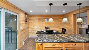 A wooden interior with a kitchen area featuring a marble countertop, wooden cabinets, and pendant lighting.