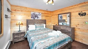A wooden-paneled bedroom with a bed, bedside tables, a mirror, and wall art.
