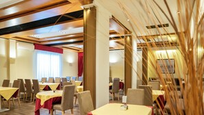 En hotellrestaurang med flera bord och stolar, en röd gardin och ett tak med synliga träbjälkar och infälld belysning.