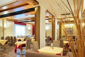 A hotel dining area with multiple tables and chairs, a red curtain, and a ceiling with wooden beams and recessed lighting. - Hotel Autoespresso Venice (Mestre)