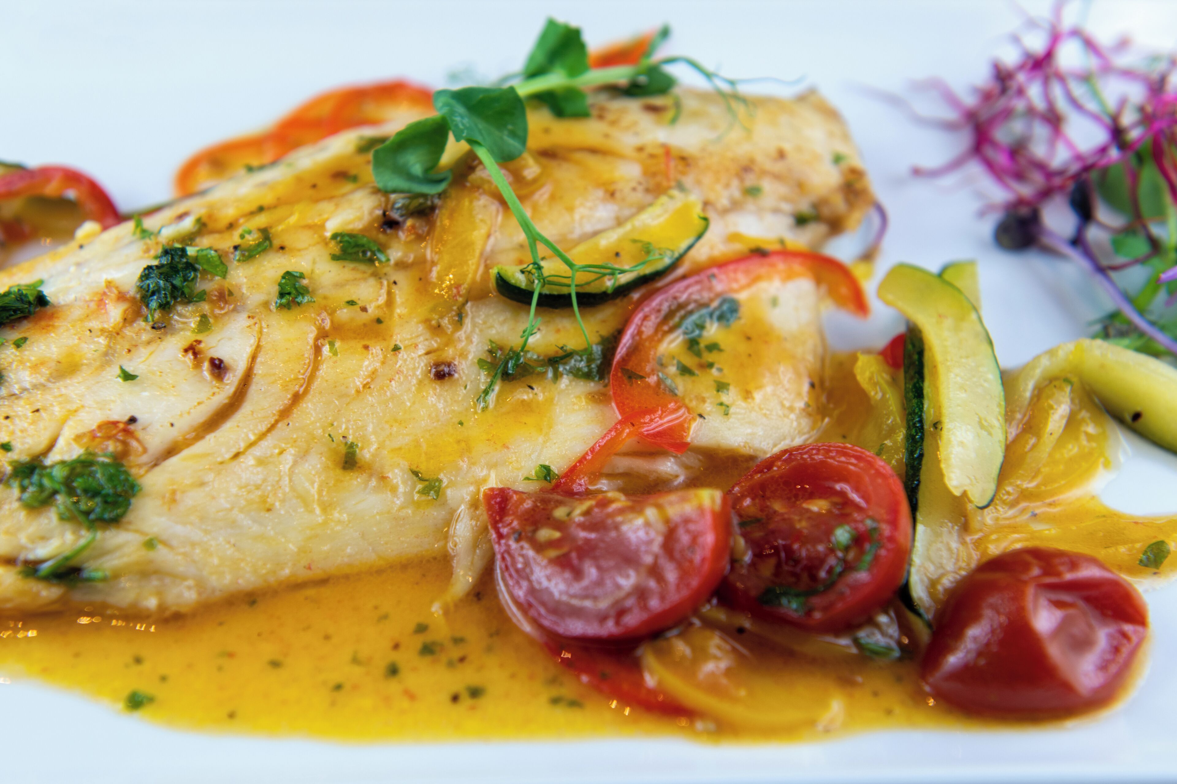 A dish with fish, tomatoes, zucchini, and greens.