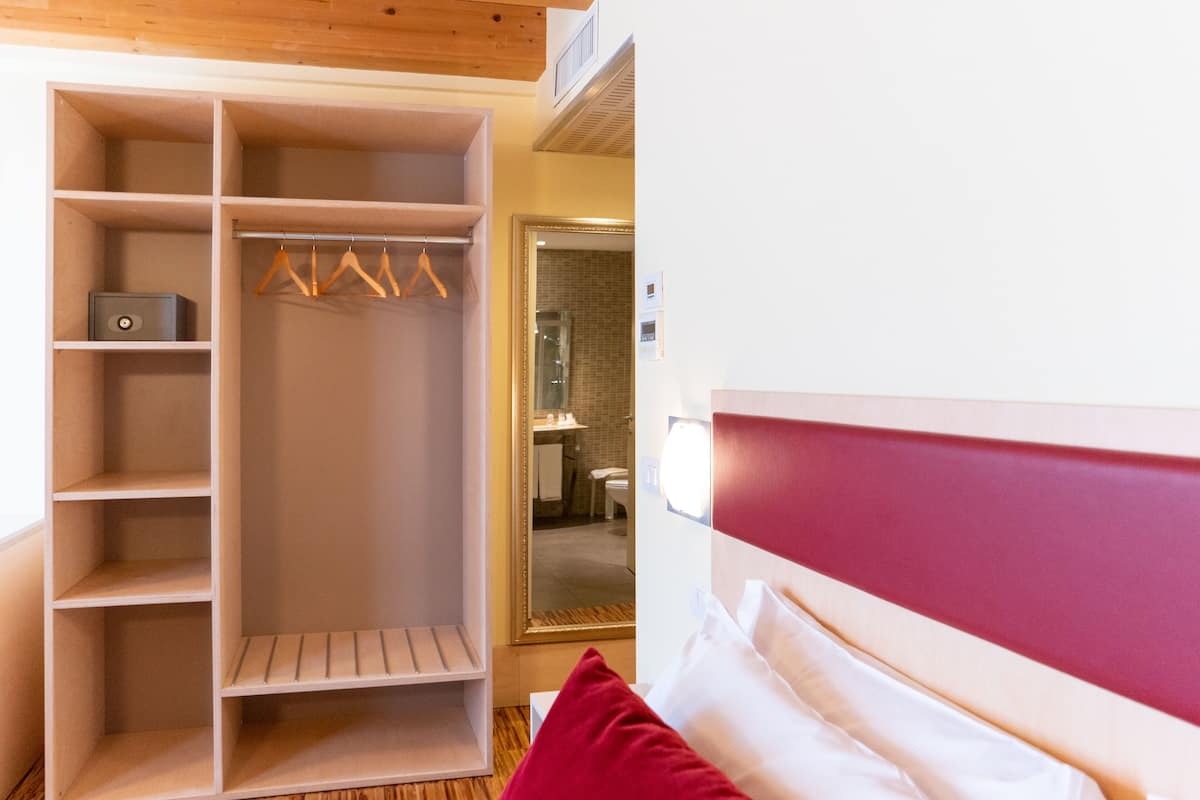 A bedroom with a bed, a wardrobe with multiple shelves, and a bathroom visible through an open door.