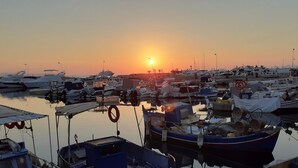 A marina with various boats docked, a sunset in the background, and calm water reflecting the boats. - Apartment 120m2 between sea and mountains in Glyfada, Athens Riviera (Glifada)