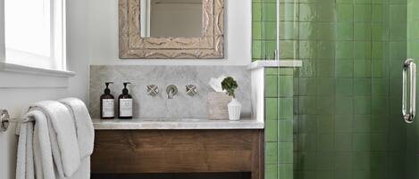 A bathroom with a green tiled shower, a white sink with a marble countertop, a wooden vanity, and a large mirror with a decorative frame.