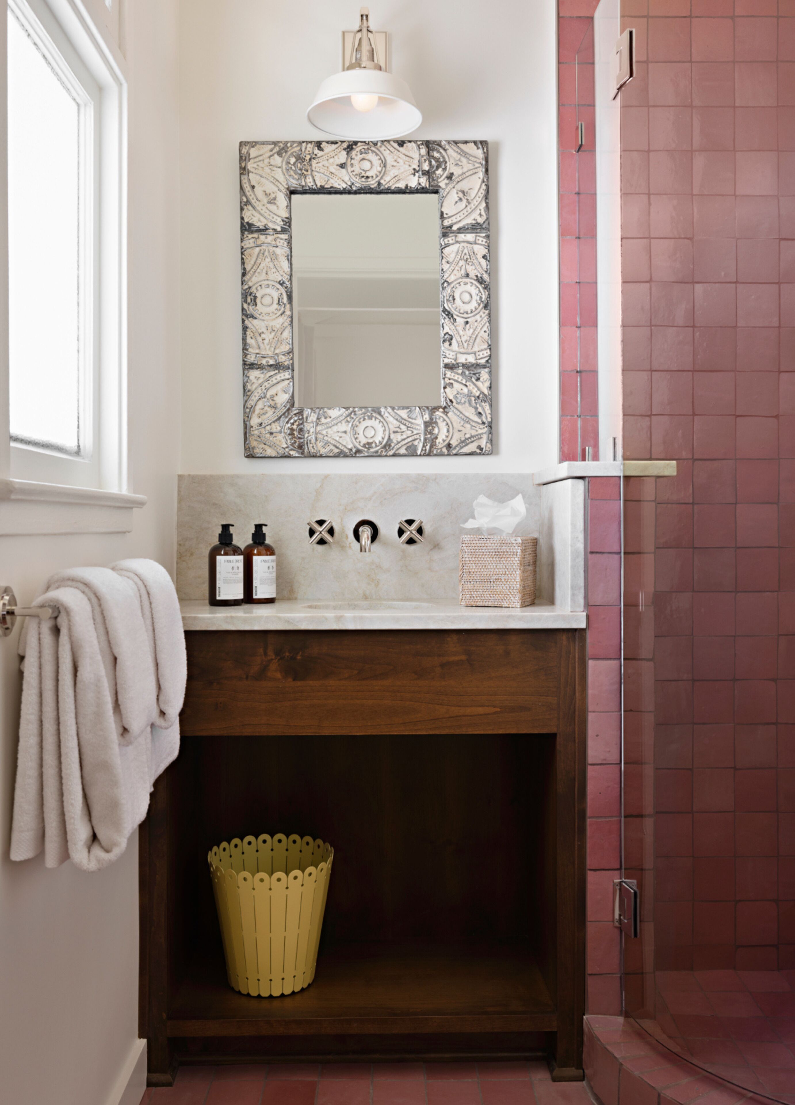 A bathroom with a white vanity, a mirror with a decorative frame, a towel rack, a sink with soap dispensers, and a yellow waste basket.