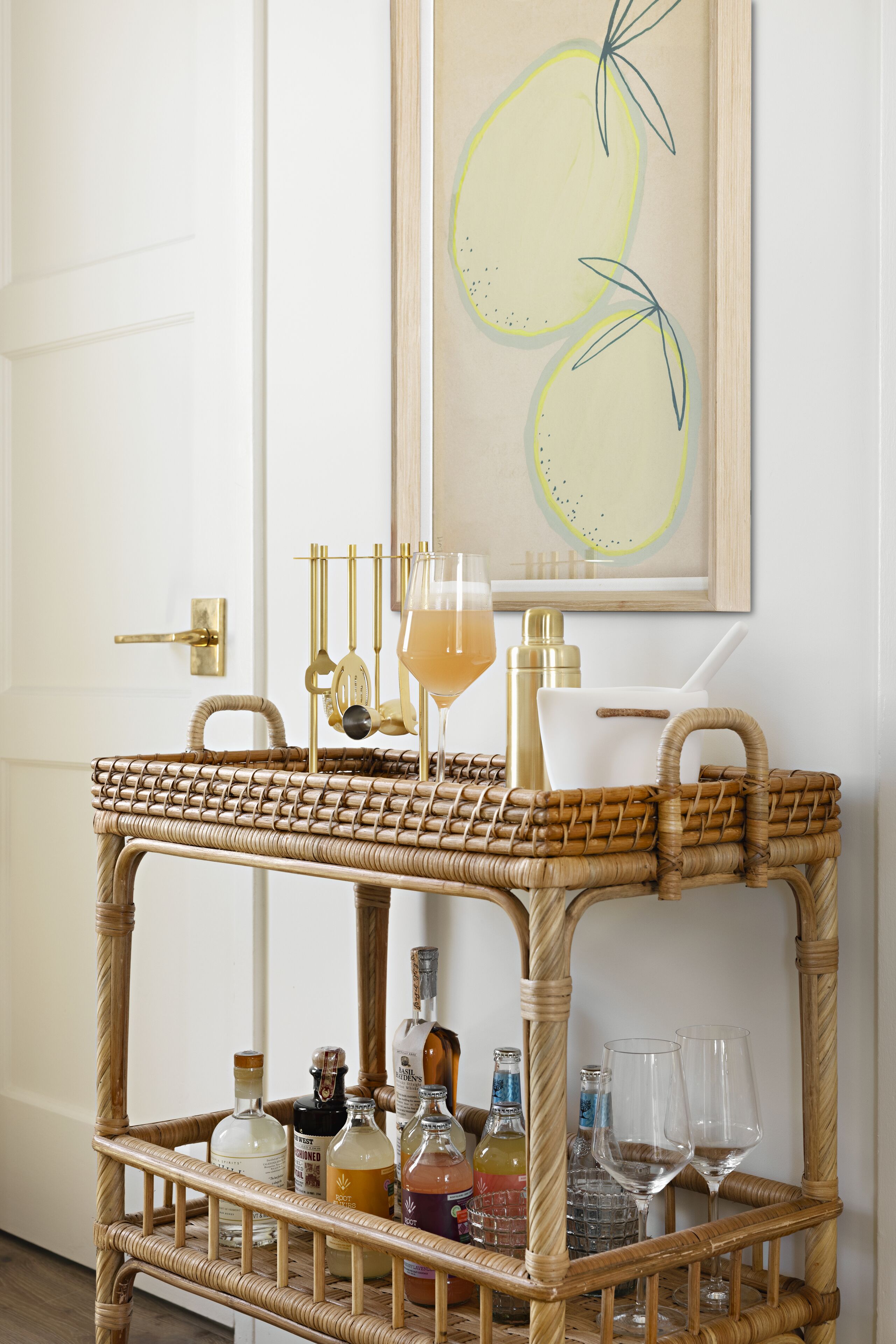 A wicker cart with bottles and glasses, a framed artwork, and a door in the background.