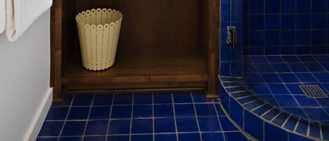A bathroom with a white vanity, a blue-tiled shower, and a wooden cabinet below the sink.