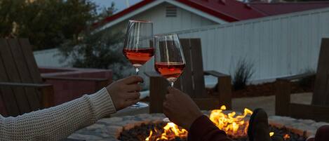 Deux personnes trinquent avec des verres de vin près d’un foyer, avec une enseigne indiquant « Farmhouse Motel » en arrière-plan.