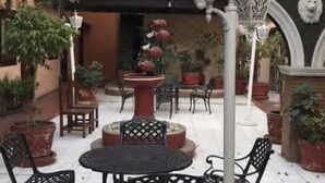 An outdoor patio with a round table, chairs, potted plants, and decorative lanterns. - Hotel San Agustin (Puebla)
