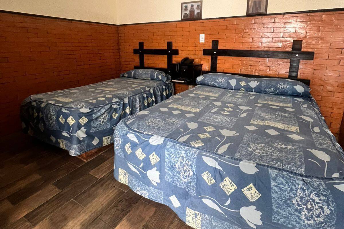 A room with two beds, wooden flooring, brick wall, and a tiled ceiling.