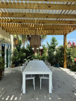 Eine Terrasse im Freien mit einer Holz-Pergola, einem weißen Tisch und Stühlen.