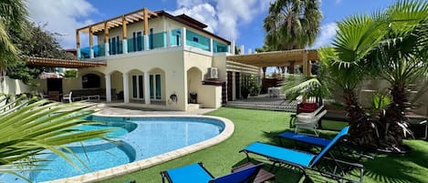 A pool area with a circular pool, blue lounge chairs, and a two-story building with a balcony.