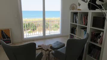 A living room with a view of the beach, a bookshelf, and two chairs.