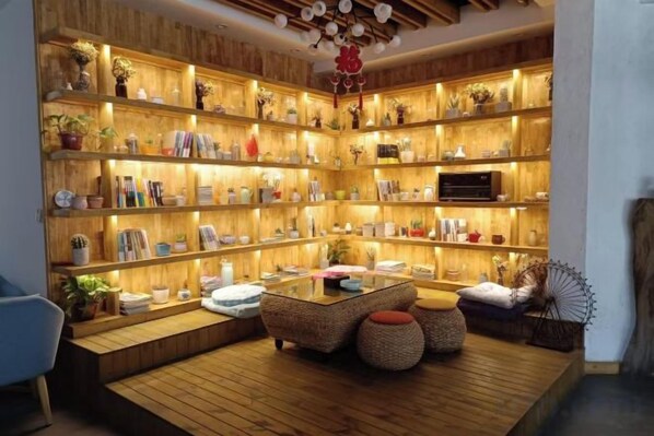 A cozy reading nook with a wooden bookshelf, a comfortable seating area, and a small table. - Jacky's Guesthouse (Yuanyang)