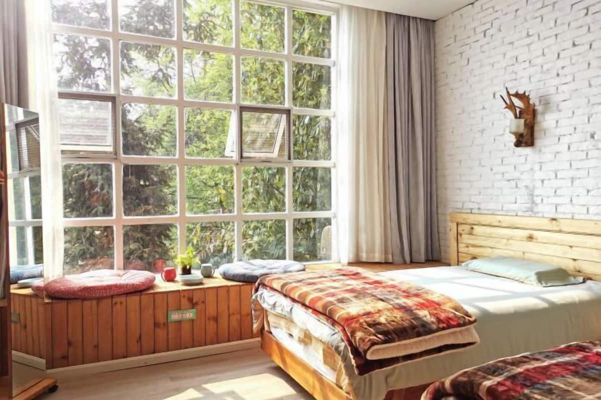 A room with a large window, wooden bench seating, a bed, and a brick wall.