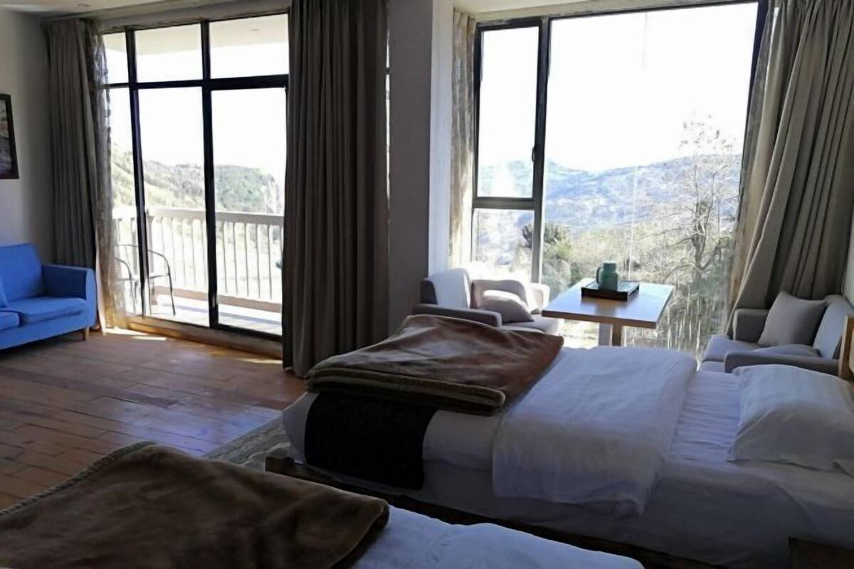 A hotel room with two beds, a blue sofa, a small table, and large windows with a view of the outdoors.