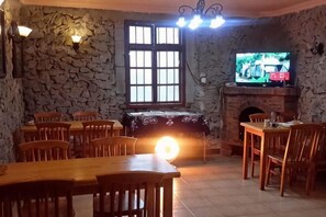 Un comedor con paredes de piedra, chimenea, televisor y varias mesas y sillas de madera.