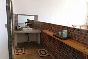 Un baño estrecho con un lavamanos blanco, un espejo y un mueble de tocador de madera con frascos.