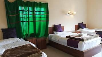 Quarto de hotel com duas camas, cortina verde, luminária fixada na parede e um banquinho de madeira.