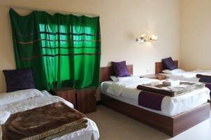 Habitación de hotel con dos camas, una cortina verde, un aplique de pared y un taburete de madera.