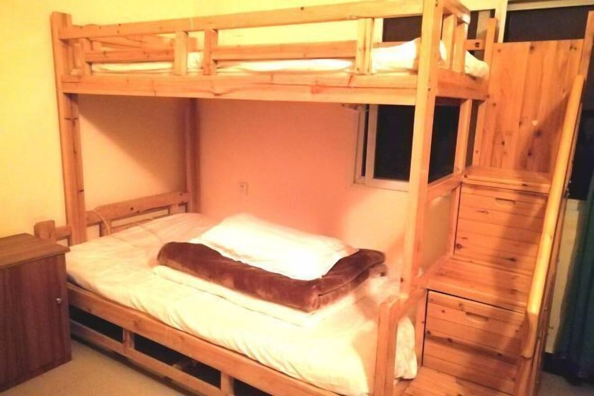 A bunk bed with a wooden headboard, a small window, and a wooden dresser.