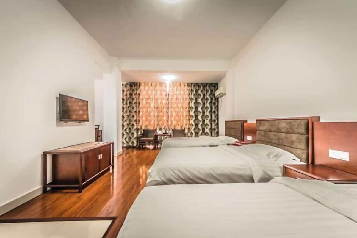 A hotel room with two beds, a wooden floor, a desk, a chair, and a TV on the wall.