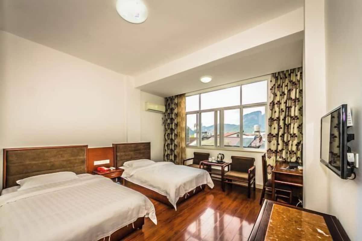 A hotel room with two beds, a small table, a chair, a TV, and a window with a view.