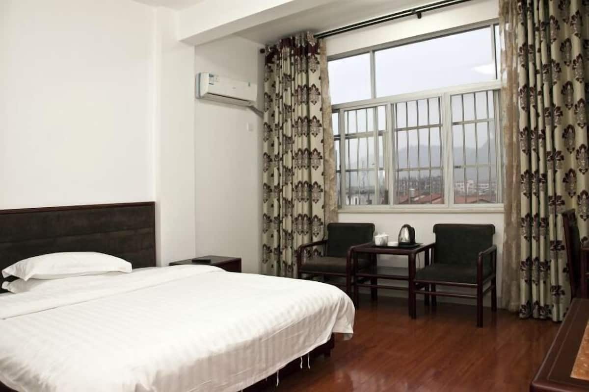 A hotel room with a large bed, two chairs, a small table, and a window with curtains.