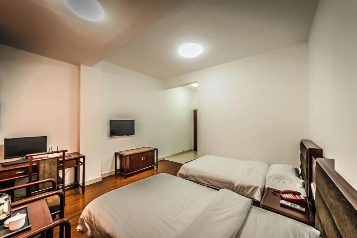 A hotel room with two beds, a desk with a chair, a television, and a small cabinet.