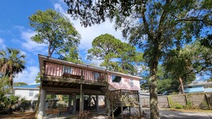 A two-story house with a balcony, surrounded by trees and a clear sky. - Tybee Pink House (Military & Veteran Discount) (Tybee Island)